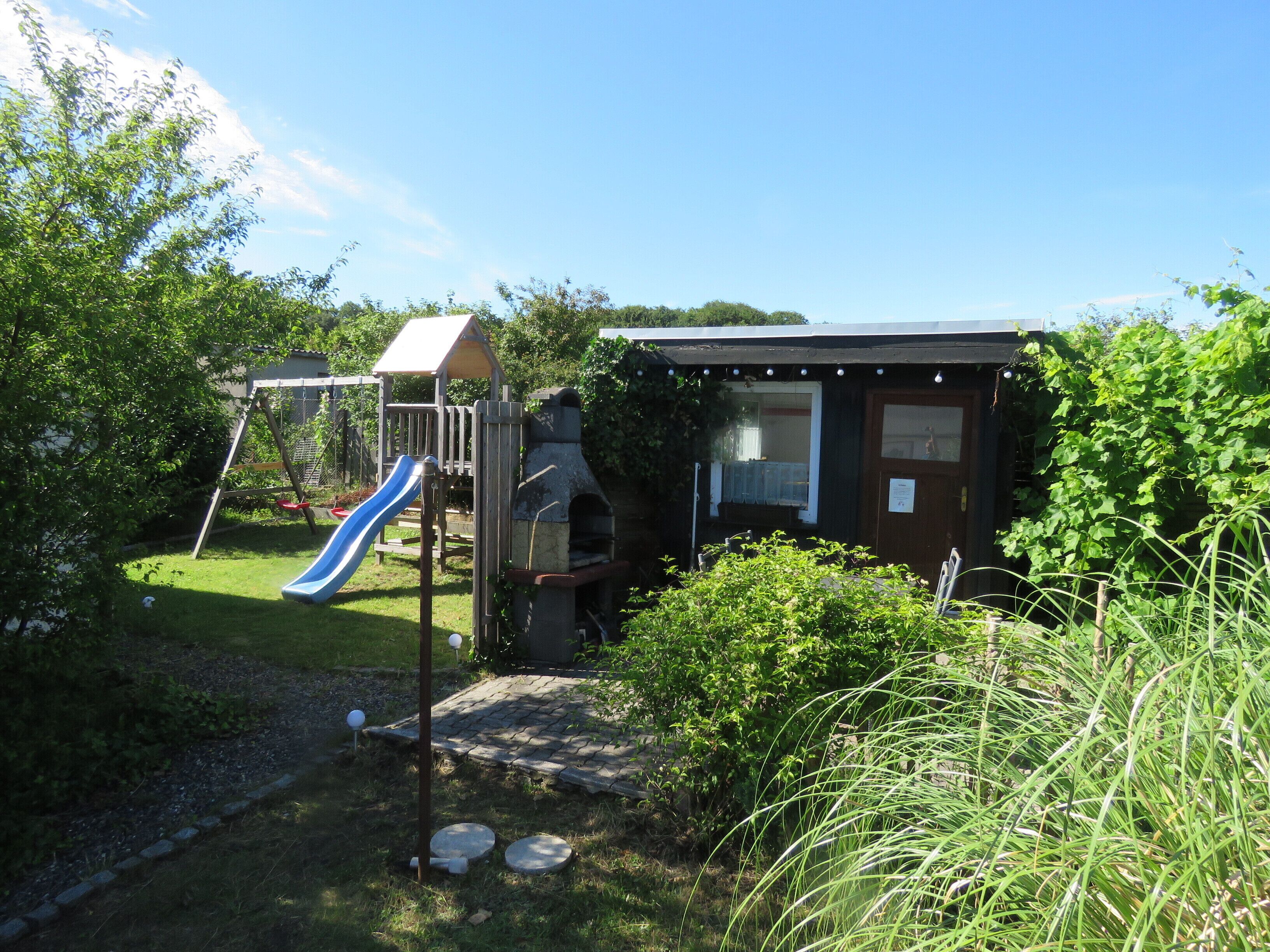 A children's play area with a slide and climbing structures, surrounded by greenery.