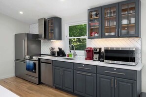A modern kitchen with grey cabinets, stainless steel appliances, and a window providing natural light. - Finger Lakes ~ Firepit, Spacious, Wine Country (Skaneateles)