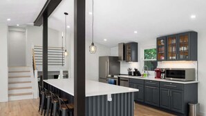 A modern kitchen with dark cabinets, a white countertop, and a bar area with stools. - Finger Lakes ~ Firepit, Spacious, Wine Country (Skaneateles)