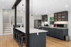 A modern kitchen with dark cabinets, a white countertop, and a bar area with stools.