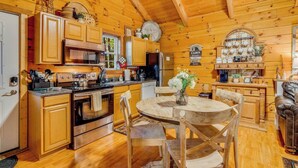 A cabin-style kitchen with wooden cabinets, a stove, and a dining area with a table and chairs. - Couples Retreat | In-Bedroom Jacuzzi, Fireplace & Private Deck · Near Helen GA (Sautee Nacoochee)