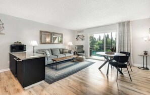 Um apartamento moderno com cozinha, sala de estar e área de jantar, com uma grande porta de vidro deslizante para uma varanda.