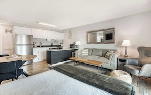 A modern apartment with a kitchenette, a sofa, a dining table, and a large bed.