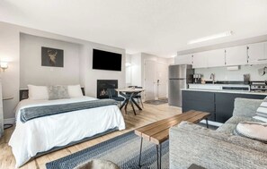 A modern hotel room with a bed, a dining table, a kitchen area, and a living space.