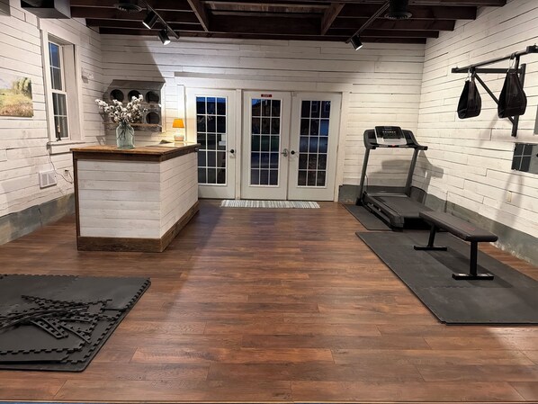 A gym with wooden flooring, exercise equipment, and a small reception area with a vase of flowers.