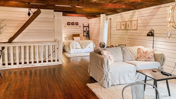 A cozy room with a wooden floor, a white bed, a sofa, and a small table.