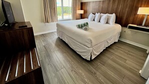 A hotel room with a large bed, a TV on a wooden stand, and a window with curtains. - Premium-Universal Studios King Bed Resort Suite, Free Parking,Full Kitchen, Pool (Orlando)