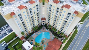 A high-rise hotel with a central swimming pool surrounded by lounge areas and palm trees. - Premium-Universal Studios King Bed Resort Suite, Free Parking,Full Kitchen, Pool (Orlando)