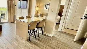 A modern hotel room with a wooden floor, a dining area with a table and chairs, a TV mounted on the wall, and a large mirror. - Premium-Universal Studios King Bed Resort Suite, Free Parking,Full Kitchen, Pool (Orlando)