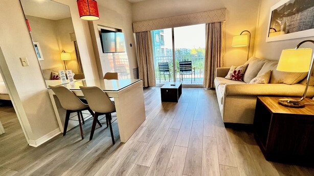 A modern hotel room with a dining area, a sofa, a TV, and a balcony with a view. - Premium-Universal Studios King Bed Resort Suite, Free Parking,Full Kitchen, Pool (Orlando)