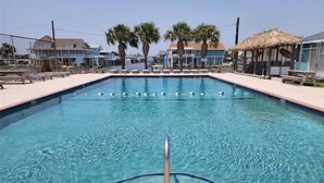 A rectangular swimming pool with clear blue water, surrounded by a brick deck. There are lounge chairs and a shaded area with a thatched roof. - "Molly”-Sea Isle w/Gulf View, Pool,yard,2 kayaks, 8min walk 2beach, Dog friendly (Galveston)