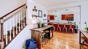 A spacious kitchen with a central island, wooden flooring, and a staircase with white railings. - Lakefront retreat for family, friends & fun! (Lake Norman of Catawba)