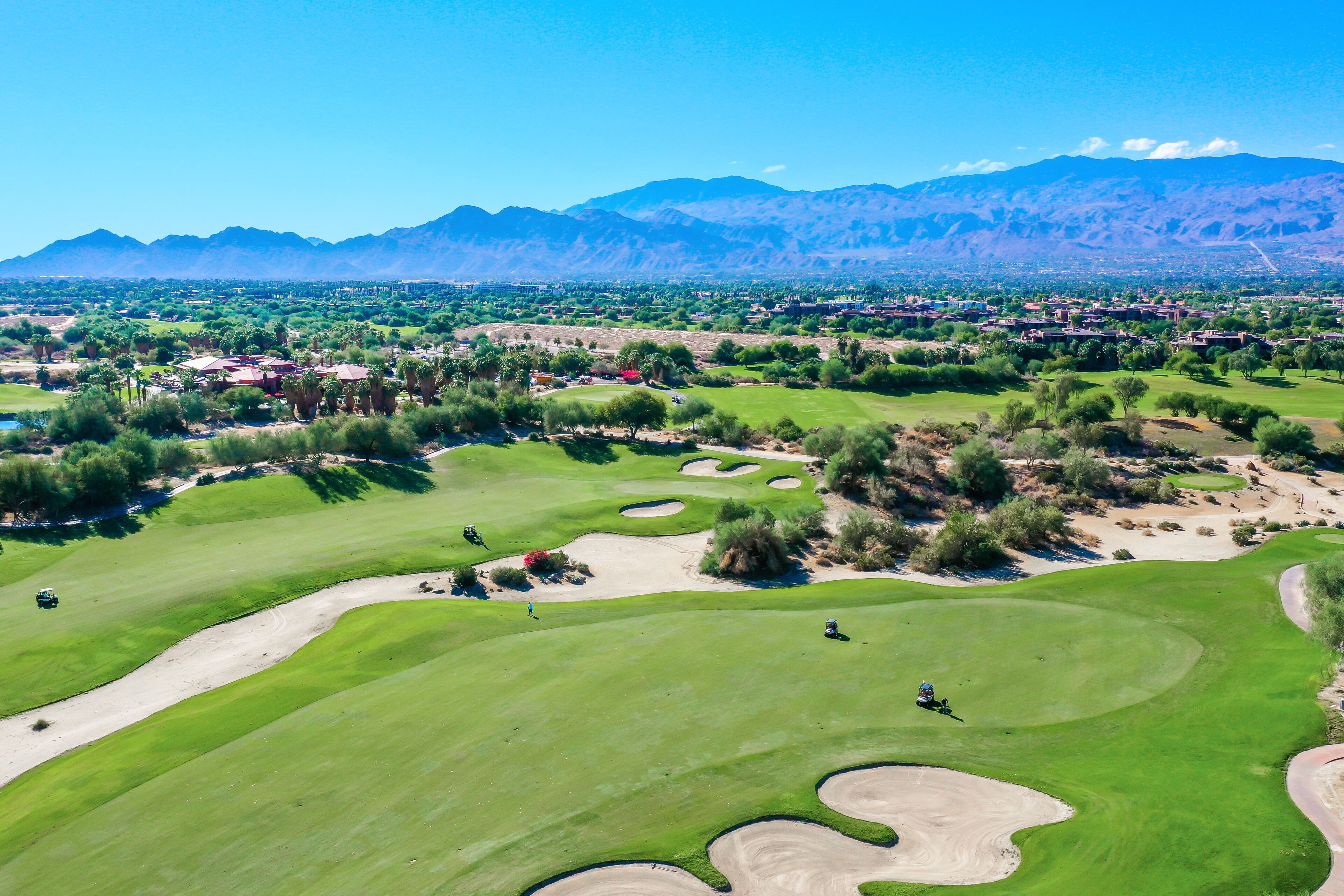 A golf course with sand bunkers, a clear sky, and mountains in the background.