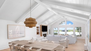 A spacious living area with a high ceiling, a dining table with chairs, a sofa, and a television. - VRBO 2025 Rental of the Year | Folly Riverfront Retreat w/ Dock & Pool (Folly Beach)