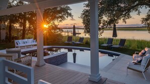 A serene outdoor patio with a pool, lounge chairs, and a view of a sunset over a body of water. - VRBO 2025 Rental of the Year | Folly Riverfront Retreat w/ Dock & Pool (Folly Beach)