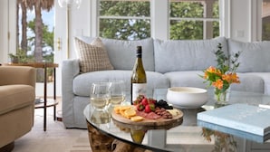 A living room with a glass table displaying a wine bottle, glasses, a fruit platter, and a book. - VRBO 2025 Rental of the Year | Folly Riverfront Retreat w/ Dock & Pool (Folly Beach)