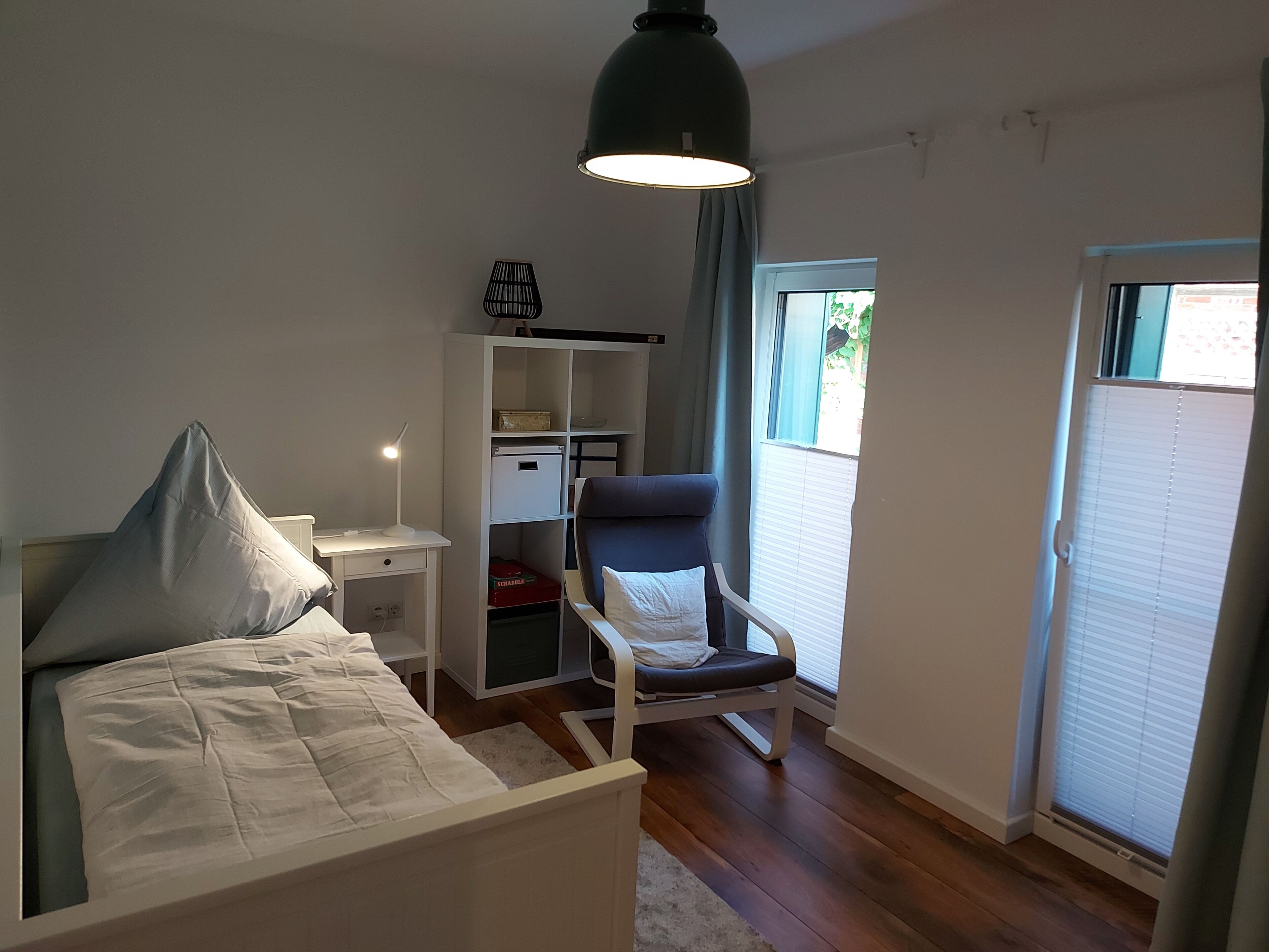 Un dormitorio con cama, mesita de noche, lámpara, silla, armario y ventana con persianas.
