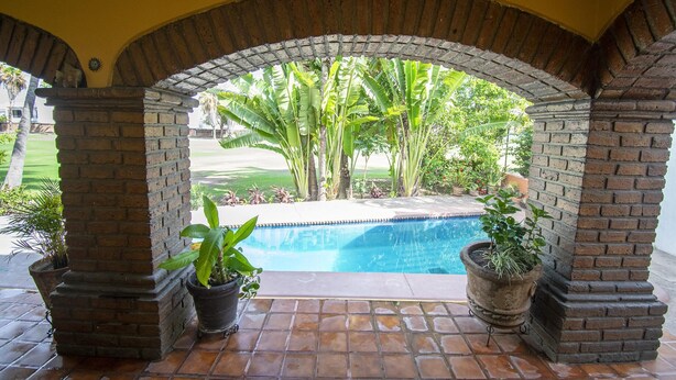 A pool area with a brick archway, potted plants, and a view of a golf course.