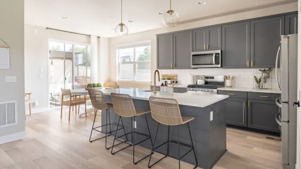 A modern kitchen with grey cabinets, a central island with bar stools, a stainless steel refrigerator, and a microwave above the island. - 4 BEDROOM MODERN HOME, FREE PARKING, A/C, W/D,WIFI (Westminster)