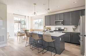 A modern kitchen with grey cabinets, a central island with bar stools, a stainless steel refrigerator, and a microwave above the island. - 4 BEDROOM MODERN HOME, FREE PARKING, A/C, W/D,WIFI (Westminster)