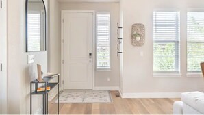A room with a white door, a small rug, a shelf with books, and a wall-mounted wreath. - 4 BEDROOM MODERN HOME, FREE PARKING, A/C, W/D,WIFI (Westminster)