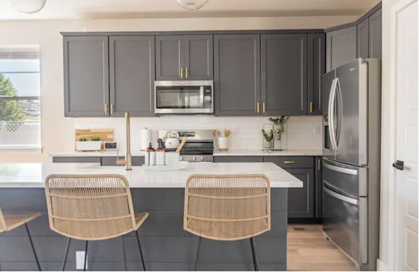 A modern kitchen with dark grey cabinets, stainless steel appliances, and a central island with two wicker chairs. - 4 BEDROOM MODERN HOME, FREE PARKING, A/C, W/D,WIFI (Westminster)