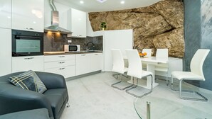 A modern kitchen with white cabinets, a built-in oven, and a dining area with white chairs and a glass table. - Hidden Gem Apartment - Two Bedroom Apartment with Terrace and Sea View (Molunat)