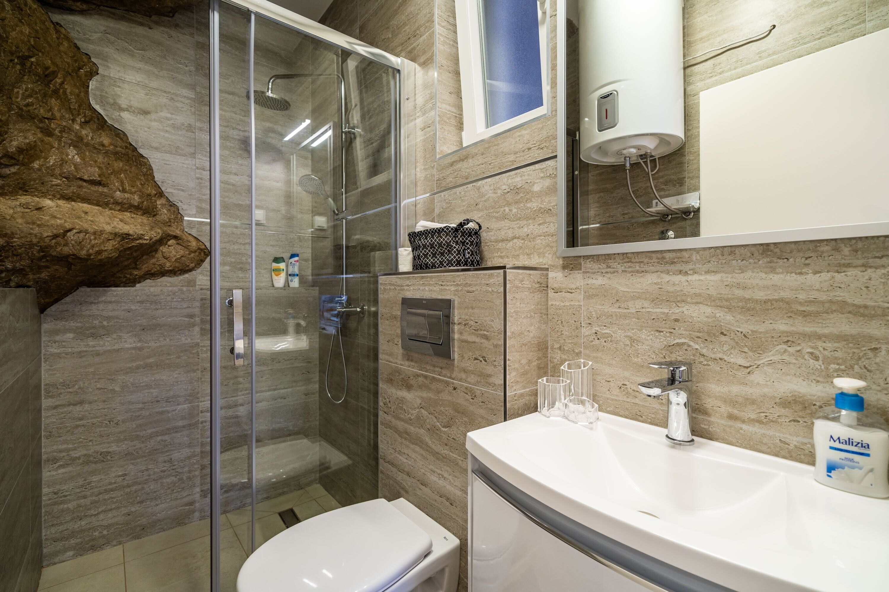 Un baño moderno con cabina de ducha de vidrio, inodoro blanco y lavamanos con espejo.