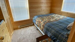 A small bedroom with a bed, a dresser, and a window. - Log Cabin by ND Badlands (Grassy Butte)