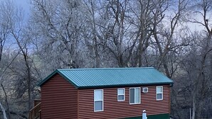A small, single-story log cabin with a green roof, surrounded by trees. - Log Cabin by ND Badlands (Grassy Butte)