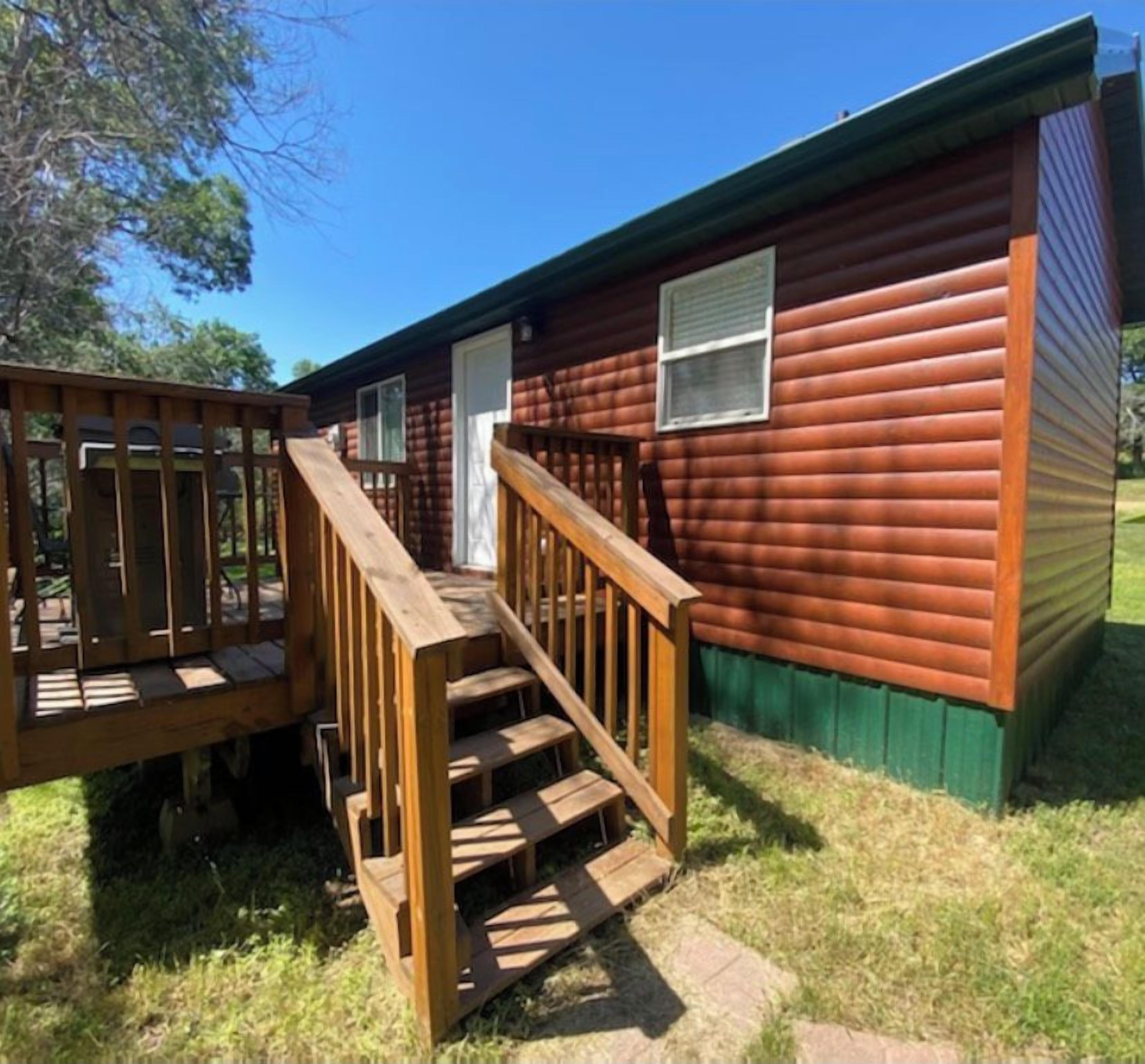 A small, single-story wooden cabin with a wooden deck and a window.