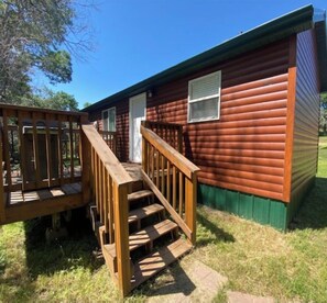 A small, single-story wooden cabin with a wooden deck and a window.