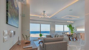 A modern living room with a large window overlooking the sea, a dining area with a view, and a cozy seating area. - seafront brand new luxury villa swimming pool -ideal for families, free transfer (Μακρύ-Γιαλός)