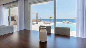 A modern hotel room with a large window overlooking a pool and the sea. - seafront brand new luxury villa swimming pool -ideal for families, free transfer (Μακρύ-Γιαλός)