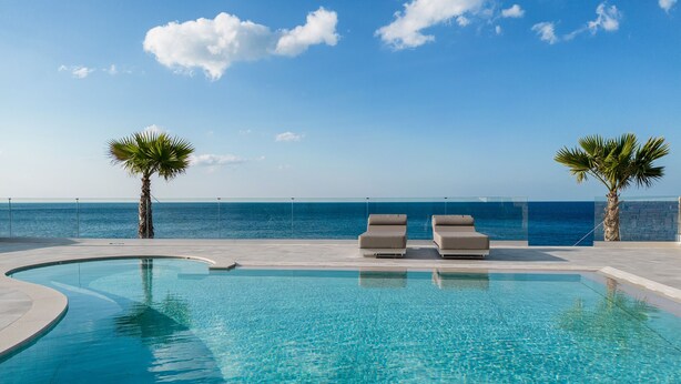 A pool with two lounge chairs and palm trees, overlooking the ocean. - seafront brand new luxury villa swimming pool -ideal for families, free transfer (Μακρύ-Γιαλός)