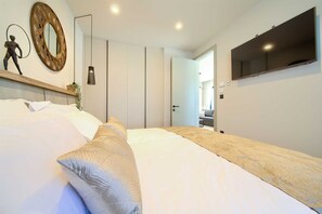 A modern bedroom with a large bed, a wall-mounted TV, and a decorative mirror.