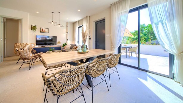 A spacious dining area with a wooden table and wicker chairs, a television, and a large window with curtains. - Villa QUARNARO with heated pool (Omišalj)