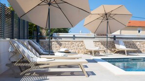 A poolside area with lounge chairs and umbrellas. - Villa QUARNARO with heated pool (Omišalj)