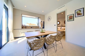 Una cocina moderna con un ventanal grande, una mesa de comedor con sillas de mimbre y un reloj en la pared.