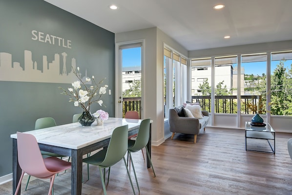 A modern living room with a dining area, large windows, and a Seattle skyline mural.