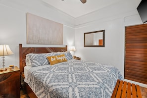Una cama bien hecha con una colcha estampada y un almohadón que dice 'be happy'.