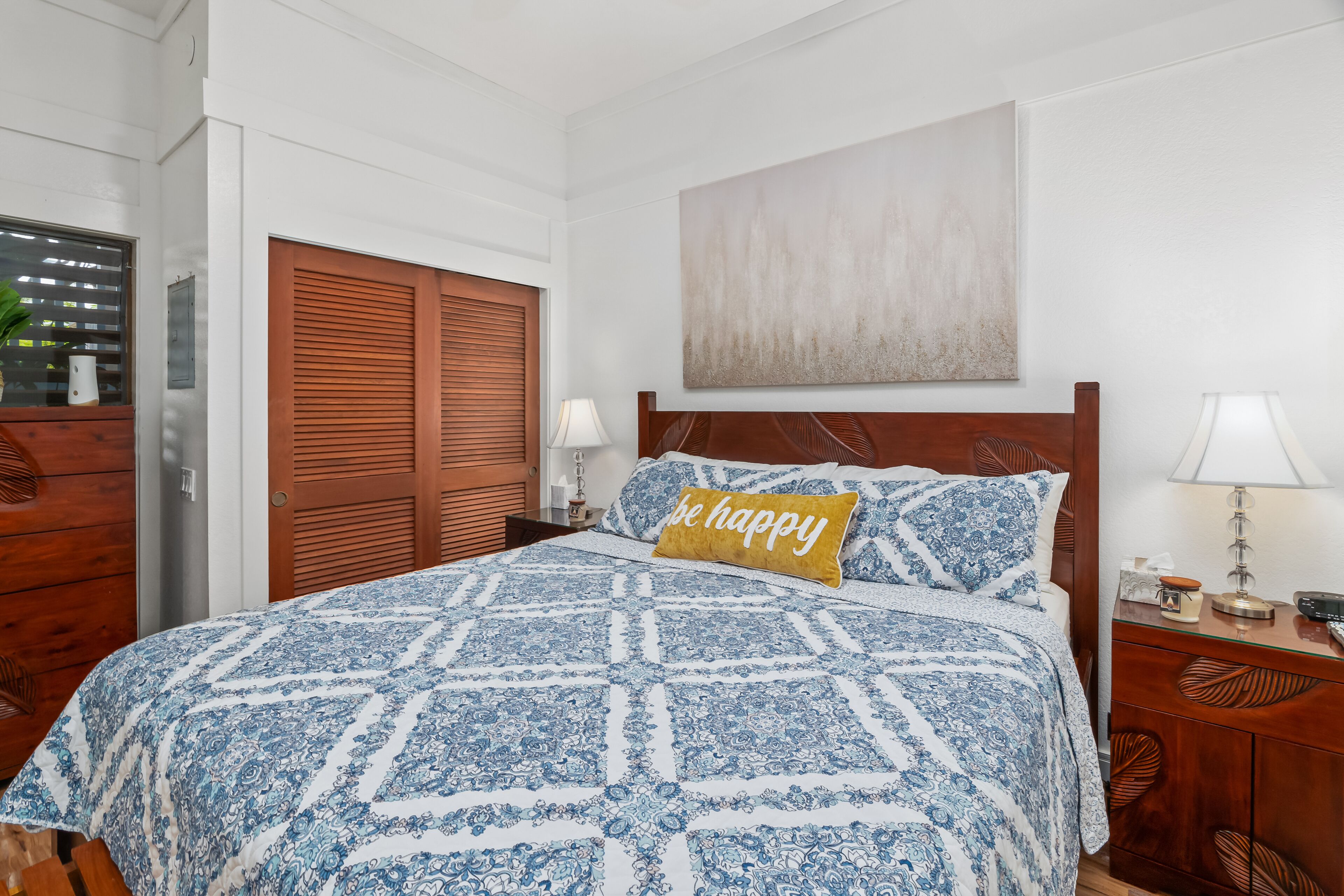 Un dormitorio con una cama grande, un armario de madera, una mesita de noche con una lámpara y una obra de arte colgada en la pared.