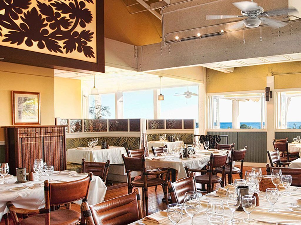 A restaurant with multiple tables and chairs, ceiling fans, and large windows with a view.