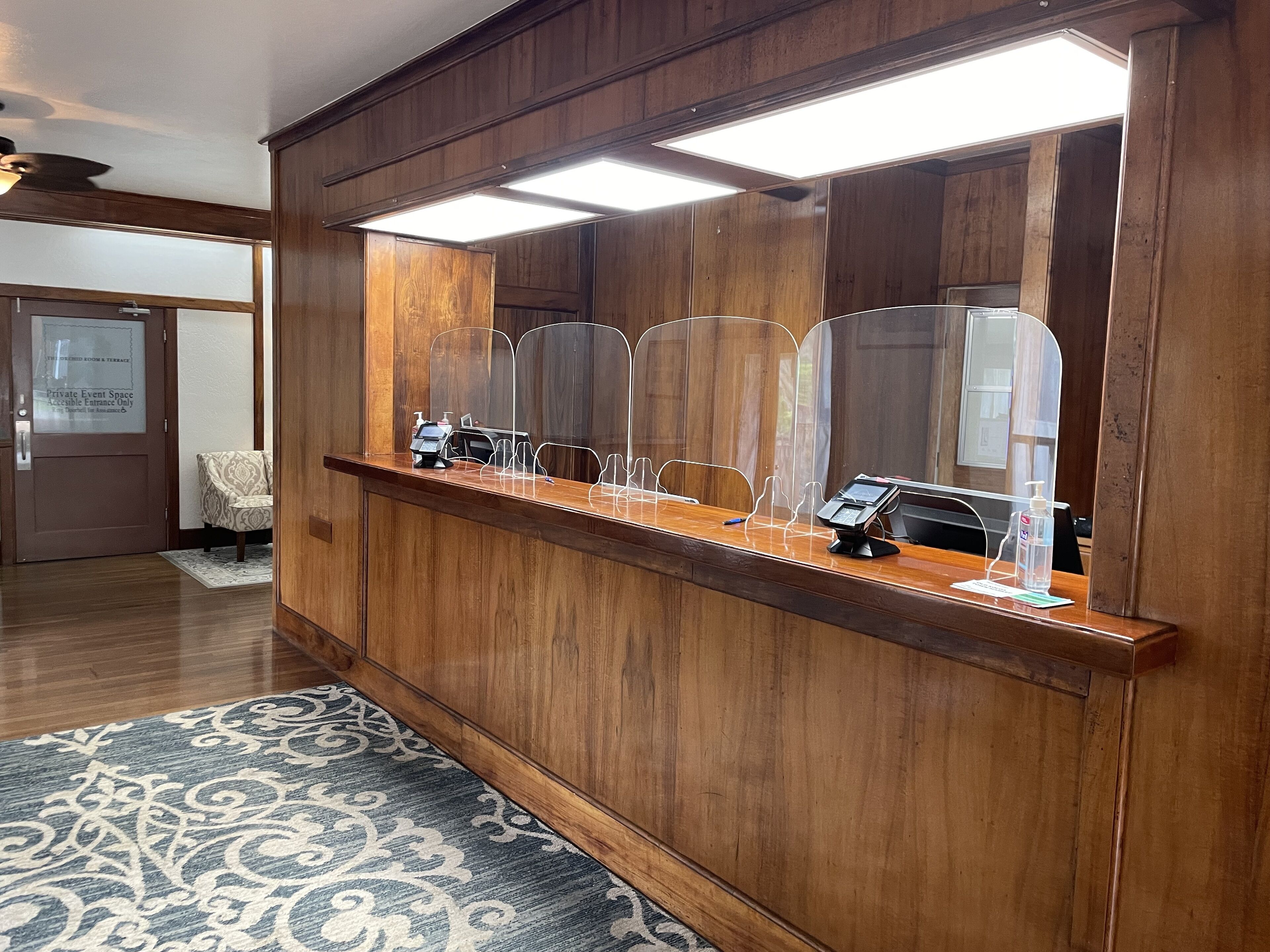 A reception desk with a wooden finish, a digital kiosk, and a glass partition.