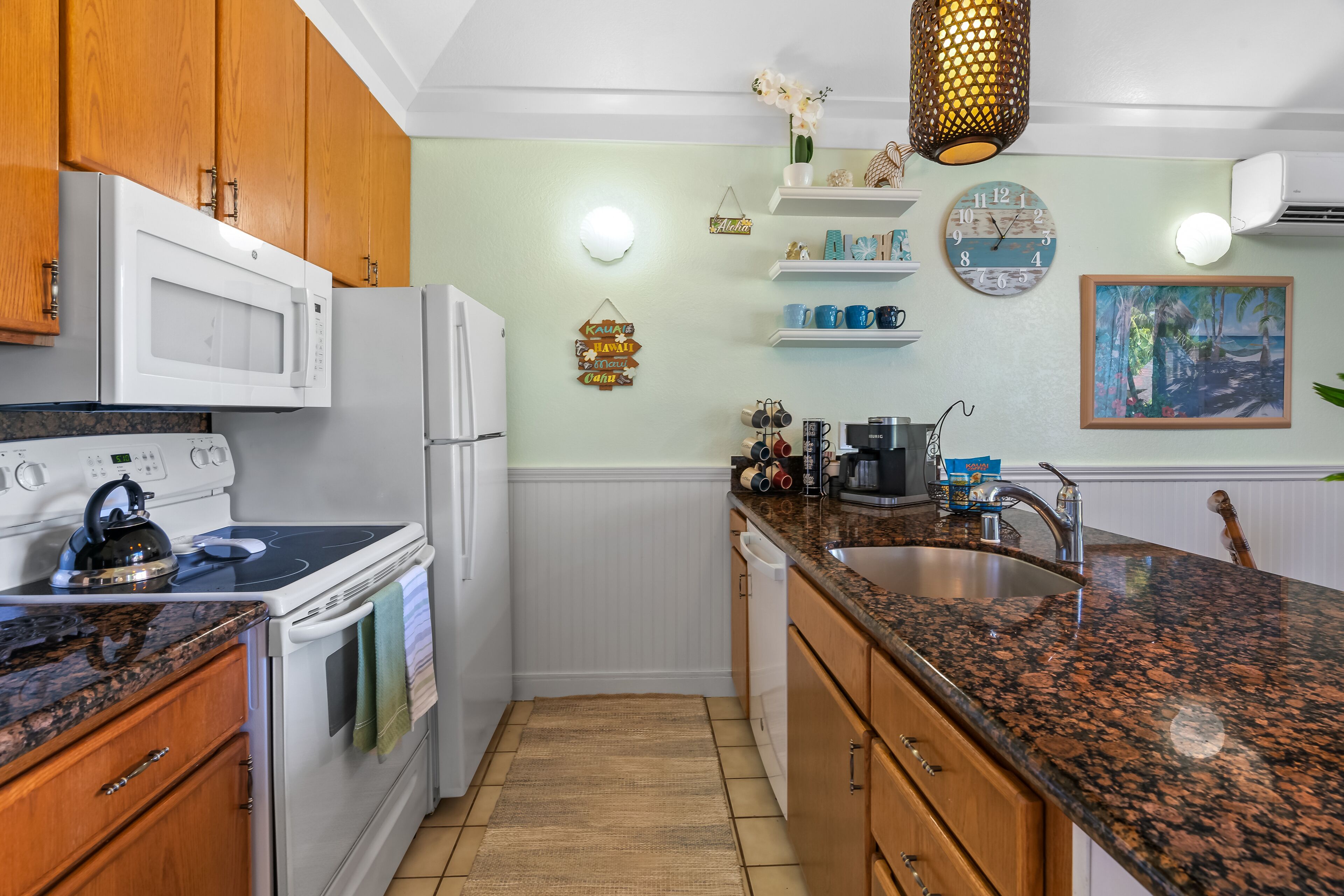 A kitchen with wooden cabinets, a granite countertop, a microwave, stove, and a sink.