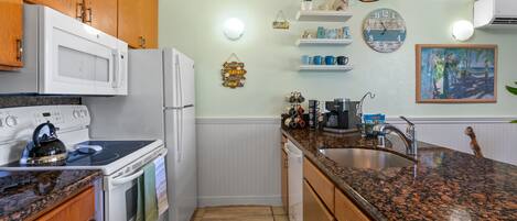 A kitchen with wooden cabinets, a granite countertop, a microwave, stove, and a sink.