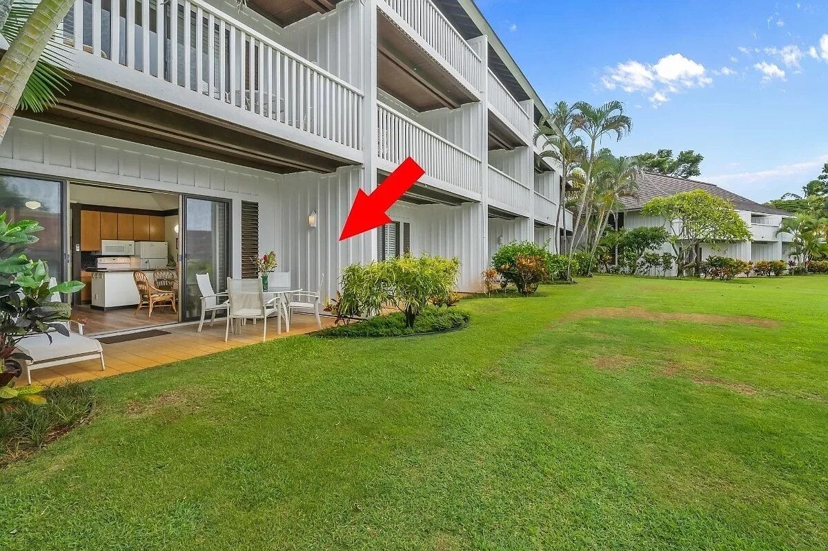 A multi-story building with a balcony, a small outdoor seating area, and a well-maintained lawn.