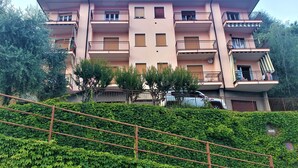 A multi-story residential building with balconies, a staircase, and a lush green hedge in the foreground. - Charming Perledo Retreat with Lake View, Balcony & Parking (Perledo)