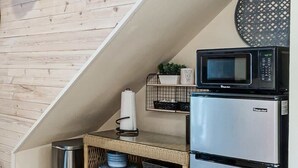 A compact kitchenette with a stainless steel refrigerator, a microwave, and a trash bin. - Studio Apartment w/ King Bed & Kitchenette (Lakeland)