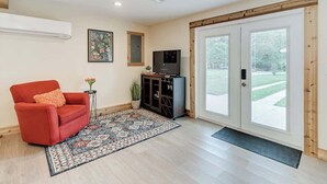 A living room with a red armchair, a television, a cabinet, and a large sliding glass door leading to an outdoor area. - Studio Apartment w/ King Bed & Kitchenette (Lakeland)